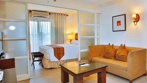 A hotel room with a bed, a sofa, a coffee table, a desk, and a chair. - Crown Regency Suites & Residences - Mactan (Lapu-Lapu)