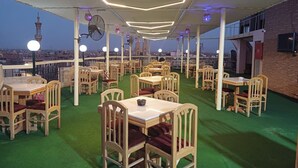 An outdoor dining area with multiple tables and chairs, a green carpet, and a view of a cityscape. - Queens Valley Hotel, Restaurants, Bars and Spa Luxor (Luxor)