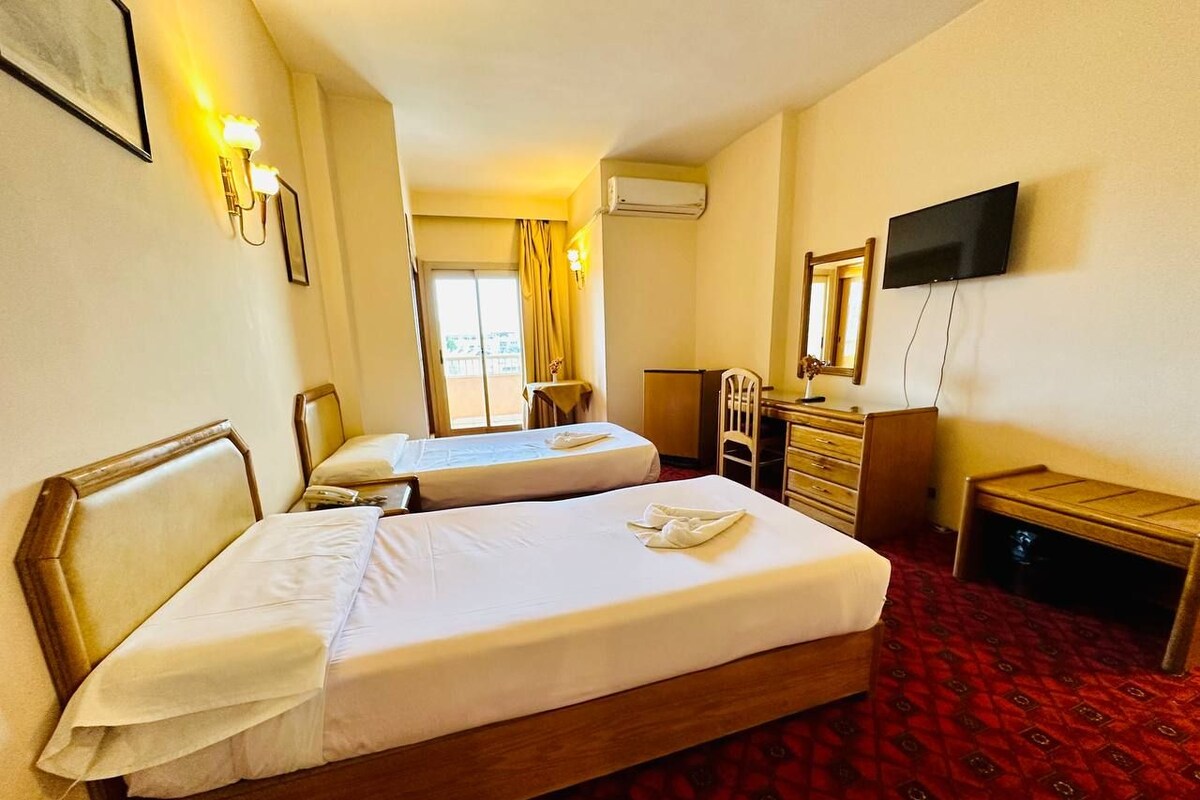 A hotel room with two beds, a desk, a chair, a television, and a window with curtains.