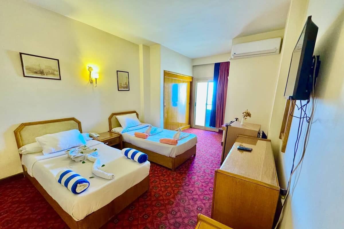 A hotel room with two beds, a desk, a TV, and a window with curtains.