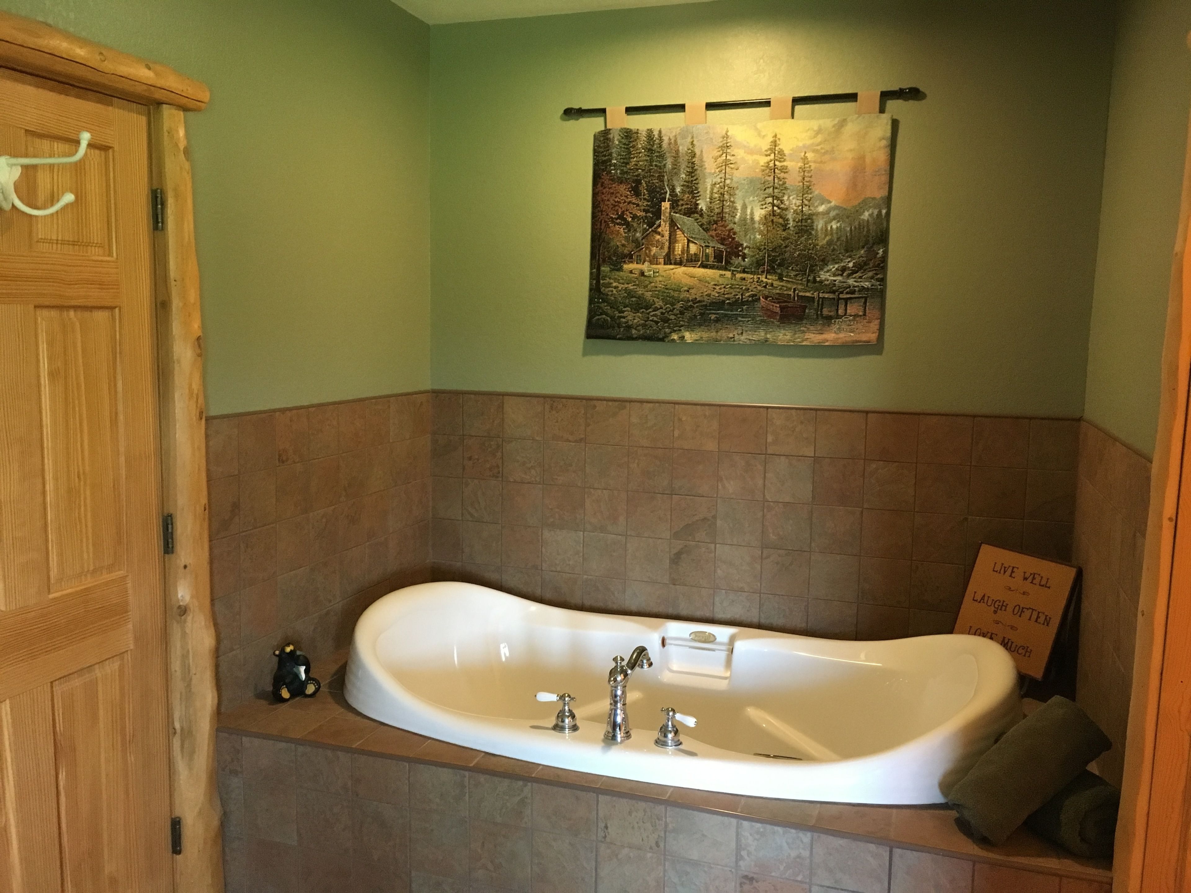 A bathroom with a freestanding bathtub, wooden cabinetry, and a painting of a forest scene on the wall.