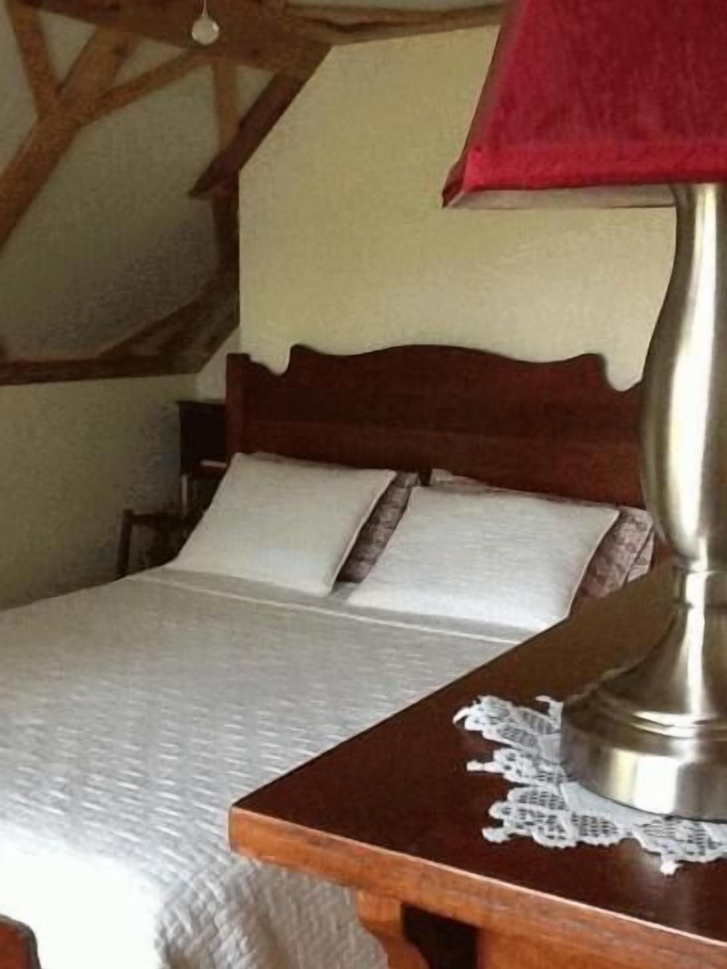 A bed with a wooden headboard, a bedside table with a lamp, and a lace doily.