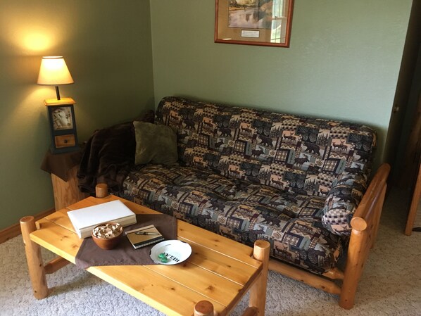 A cozy living room with a patterned sofa, a wooden coffee table with a bowl and a book, and a lamp on a side table.