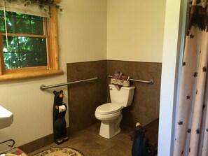 A bathroom with a toilet, a window with a view of trees, and two bear figurines.