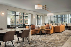 Un hall d’hôtel moderne doté d’une grande table à manger, de sièges confortables, de grandes fenêtres et offrant une vue sur la ville.
