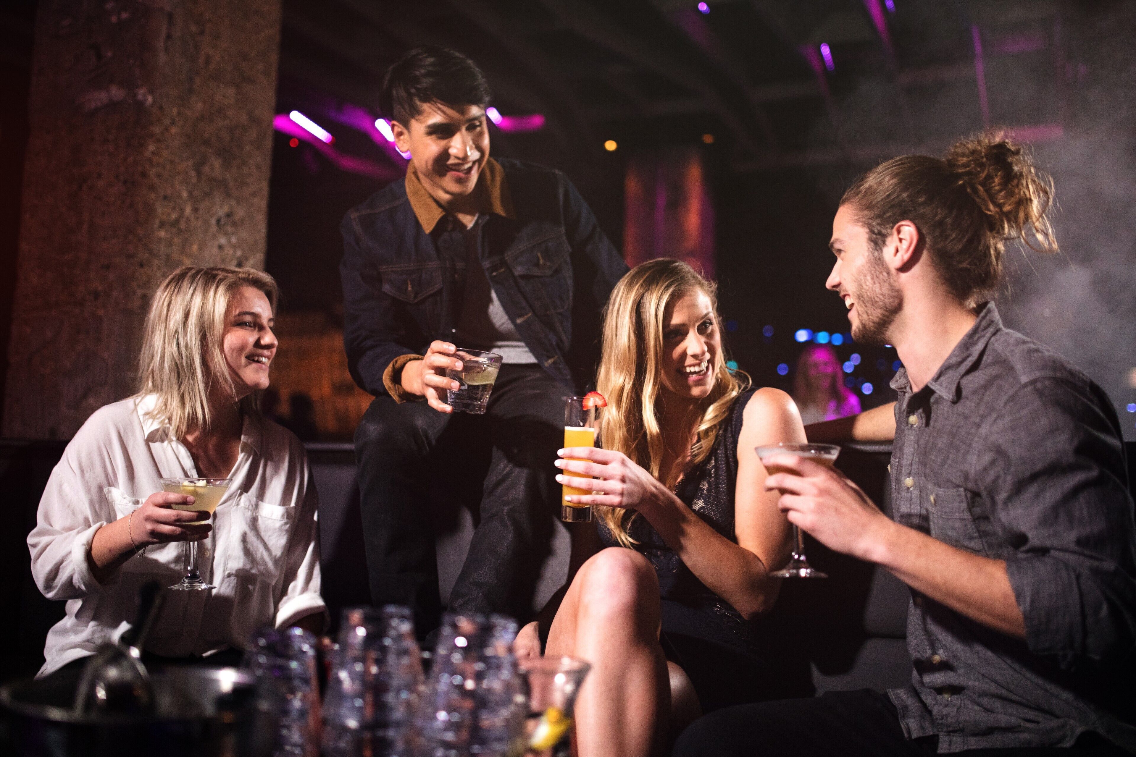 A group of people sitting around a table with drinks, in a dimly lit indoor setting.