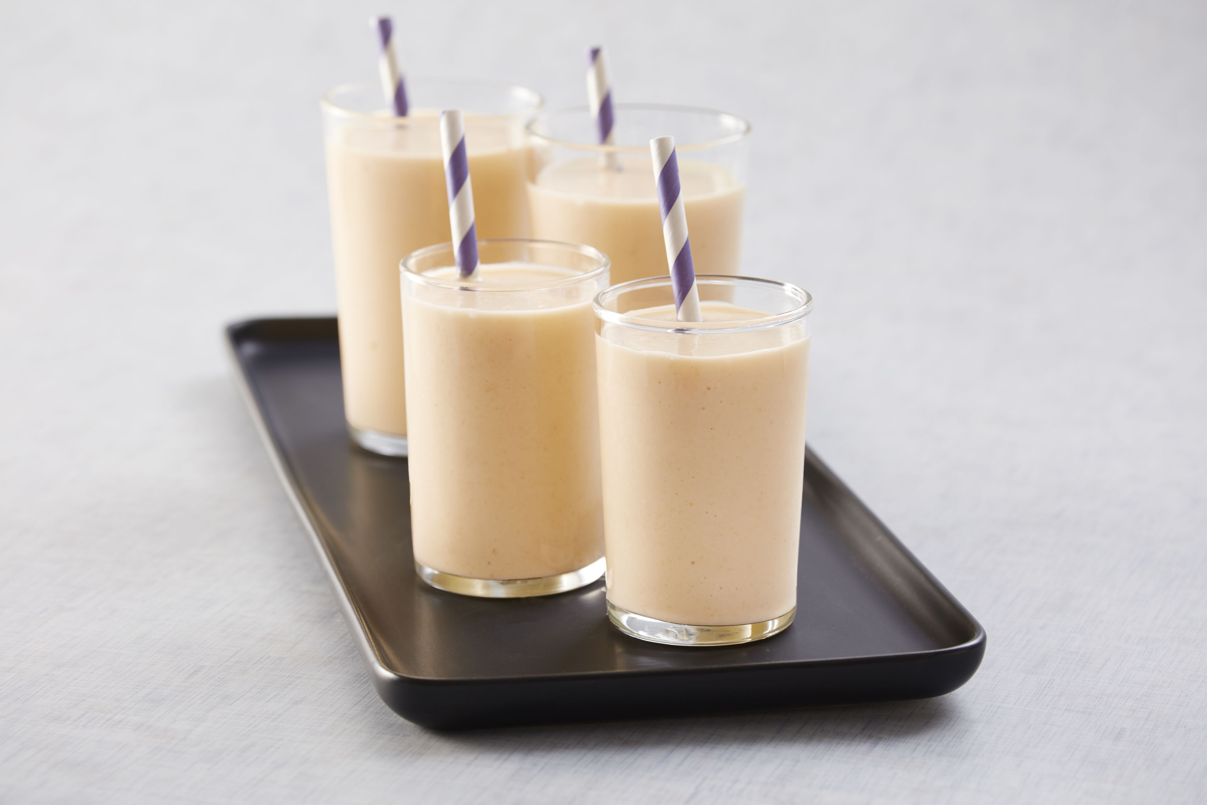 Cuatro vasos de una bebida cremosa sobre una bandeja negra.