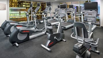 Un gimnasio con varias máquinas de cardio, incluyendo cintas de correr y elípticas, dispuestas en filas.