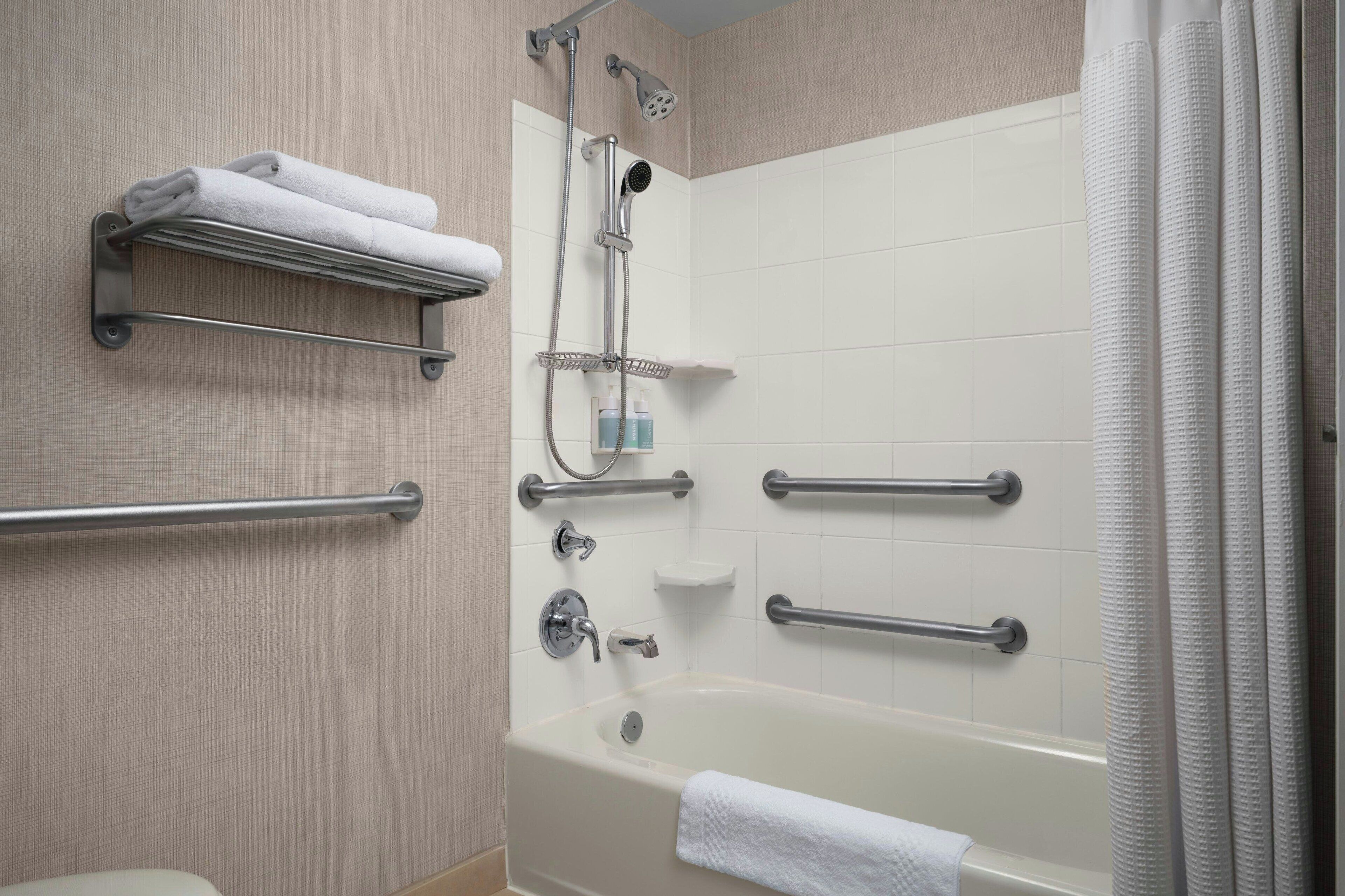 Une salle de bain moderne équipée d’une baignoire, d’une douche et de barres d’appui.