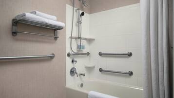 Une salle de bain moderne équipée d’une baignoire, d’une douche et de barres d’appui.