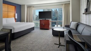 A hotel room with a bed, sofa, TV, and a view of the cityscape. - Residence Inn by Marriott Chicago Downtown / River North (Chicago)