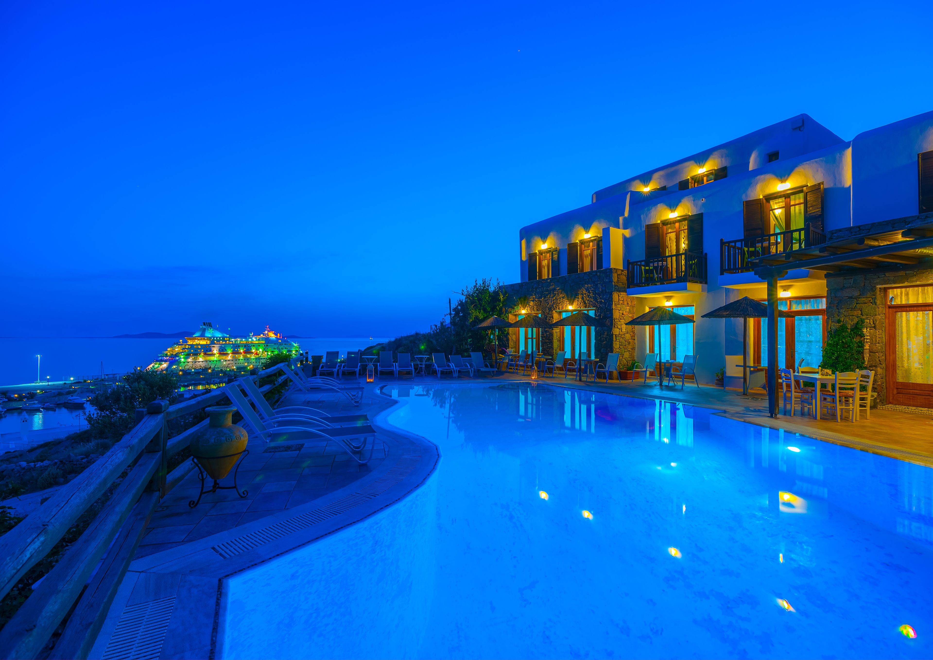 A resort with a swimming pool, lounge chairs, and a view of the sea.