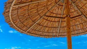 A poolside area with lounge chairs, a thatched umbrella, and a view of the sea and distant buildings.