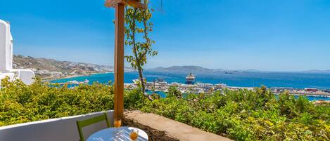 A terrace with a table and chairs, overlooking a coastal town with clear blue waters and a view of the sea.