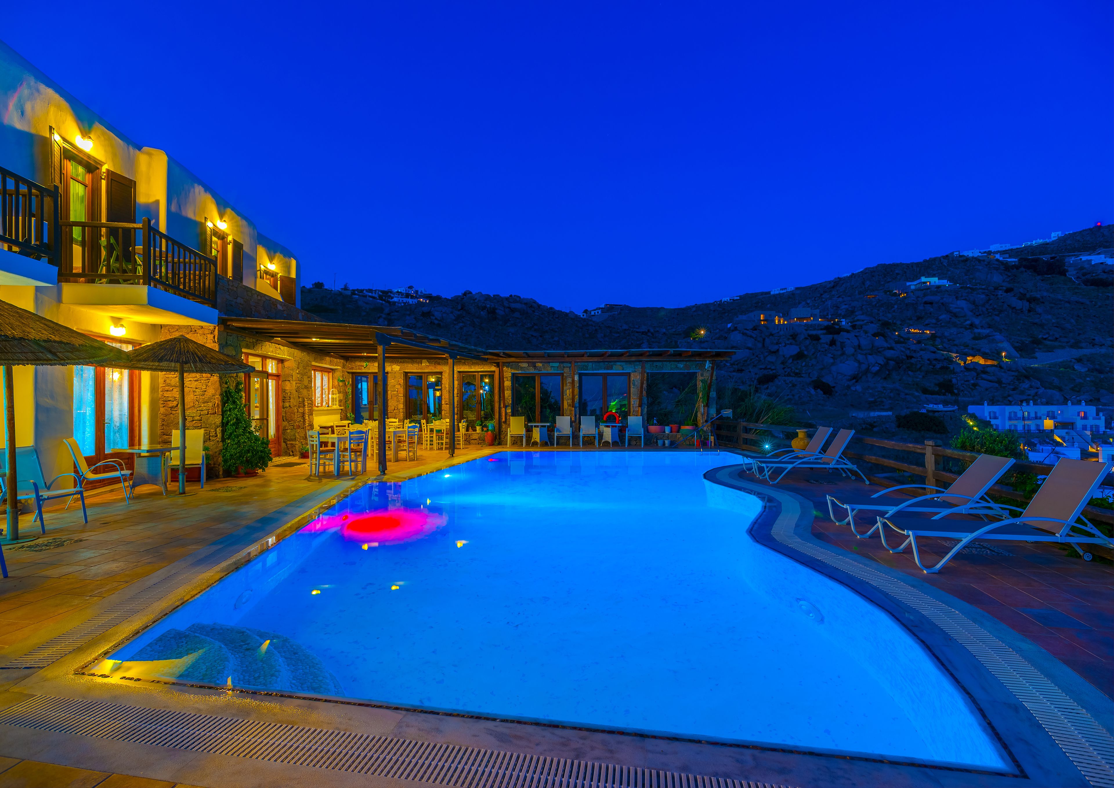 A swimming pool with lounge chairs, a covered seating area, and a building with multiple balconies.