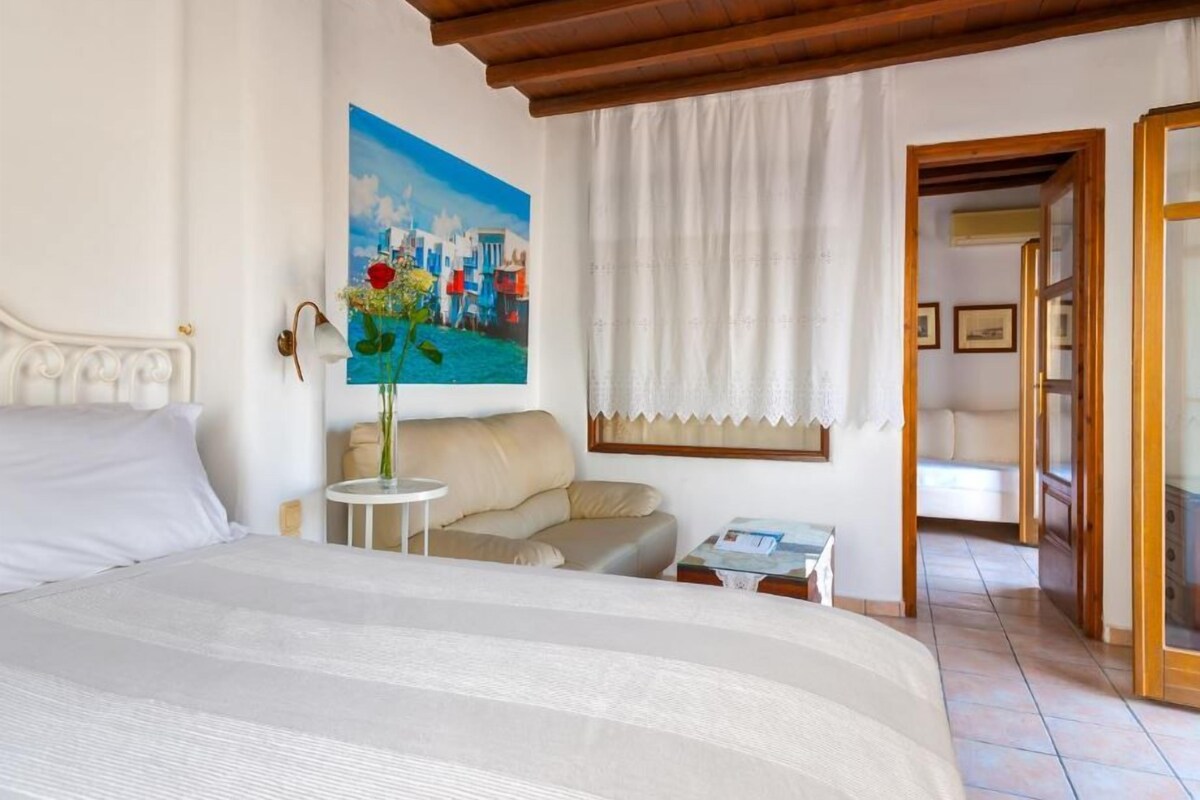 Un dormitorio con cama, sofá, una mesita, un cuadro y una puerta que da a otra habitación.