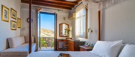 A bedroom with a bed, a desk, a chair, a window with a view of a hillside, and a balcony with a stone wall.