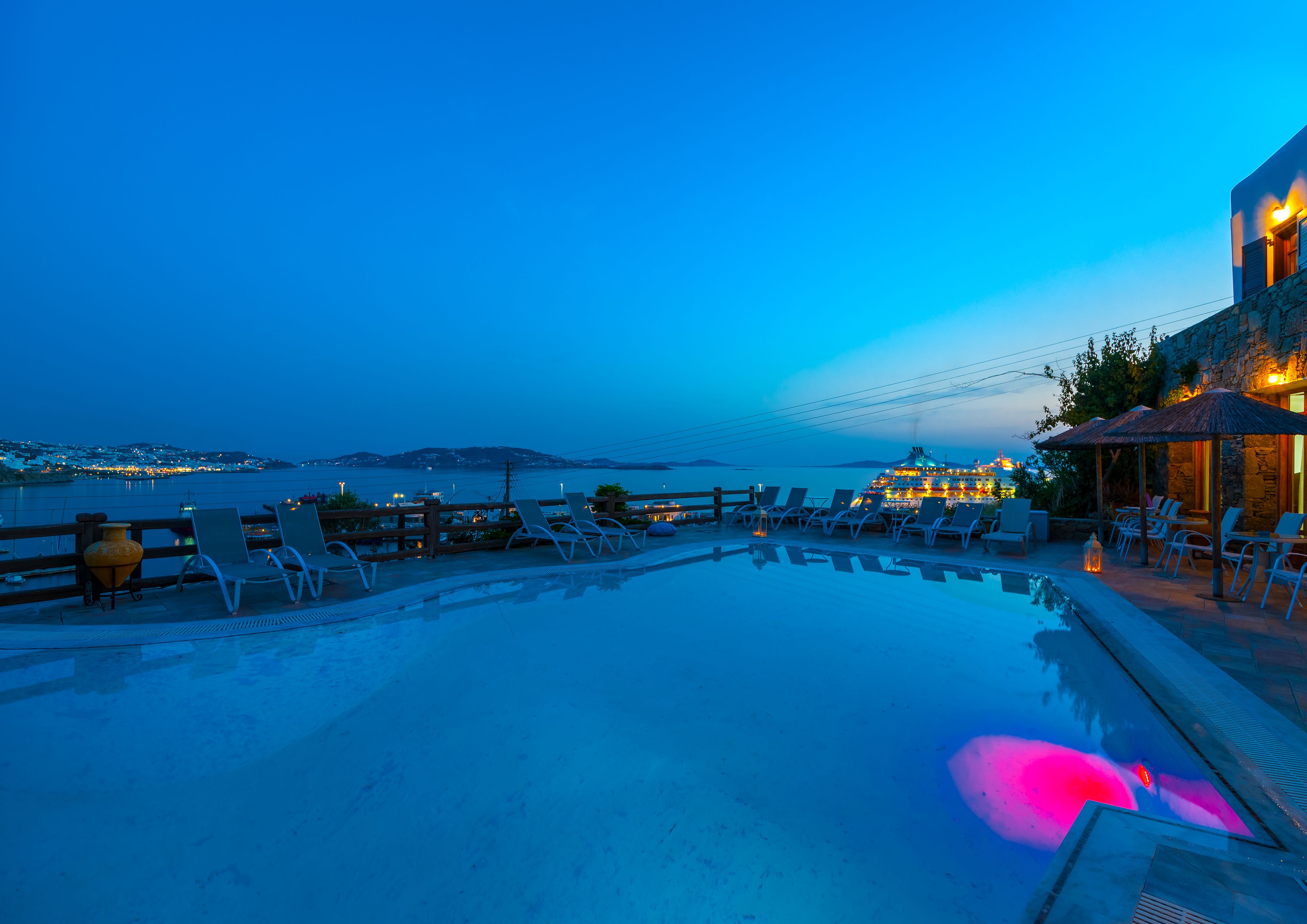 A poolside area with lounge chairs and umbrellas, overlooking a body of water and distant islands.