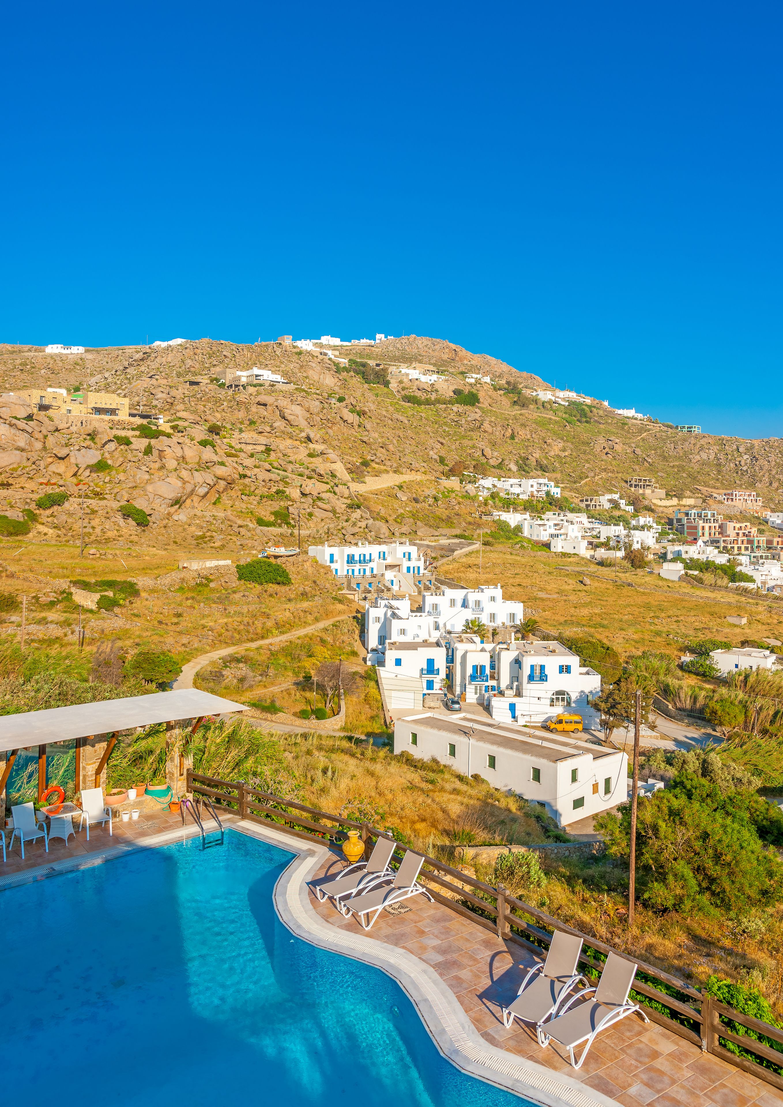 A pool area with lounge chairs and a view of white buildings on a hillside.