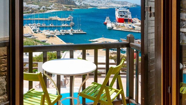 A balcony with a view of a harbor, a table, and two chairs.