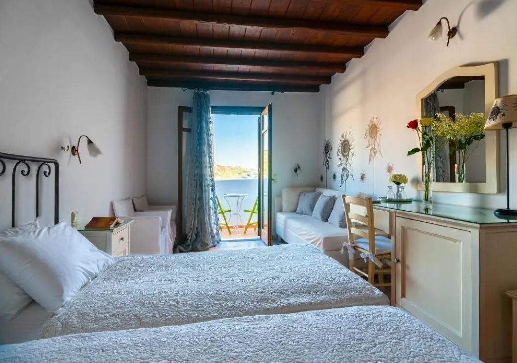 Une chambre avec deux lits, un plafond en bois, un balcon avec une table et des chaises, et une vue sur la mer.