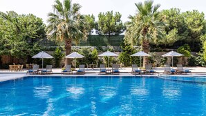 Une piscine entourée de palmiers et de verdure, avec des chaises longues et des parasols.