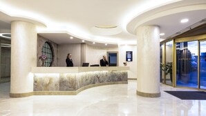 Een moderne hotel receptie met een marmeren balie, twee receptionisten en een glazen entree.