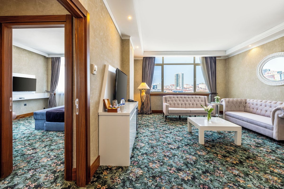 A hotel room with a sofa, a coffee table, a TV, and a view of the cityscape.