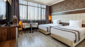 Une chambre d’hôtel avec deux lits, une télévision, une petite table avec des chaises et une fenêtre avec des rideaux.