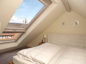 Ein Schlafzimmer mit Dachfenster, einem Bett, einem Nachttisch und zwei gerahmten Bildern an der Wand.