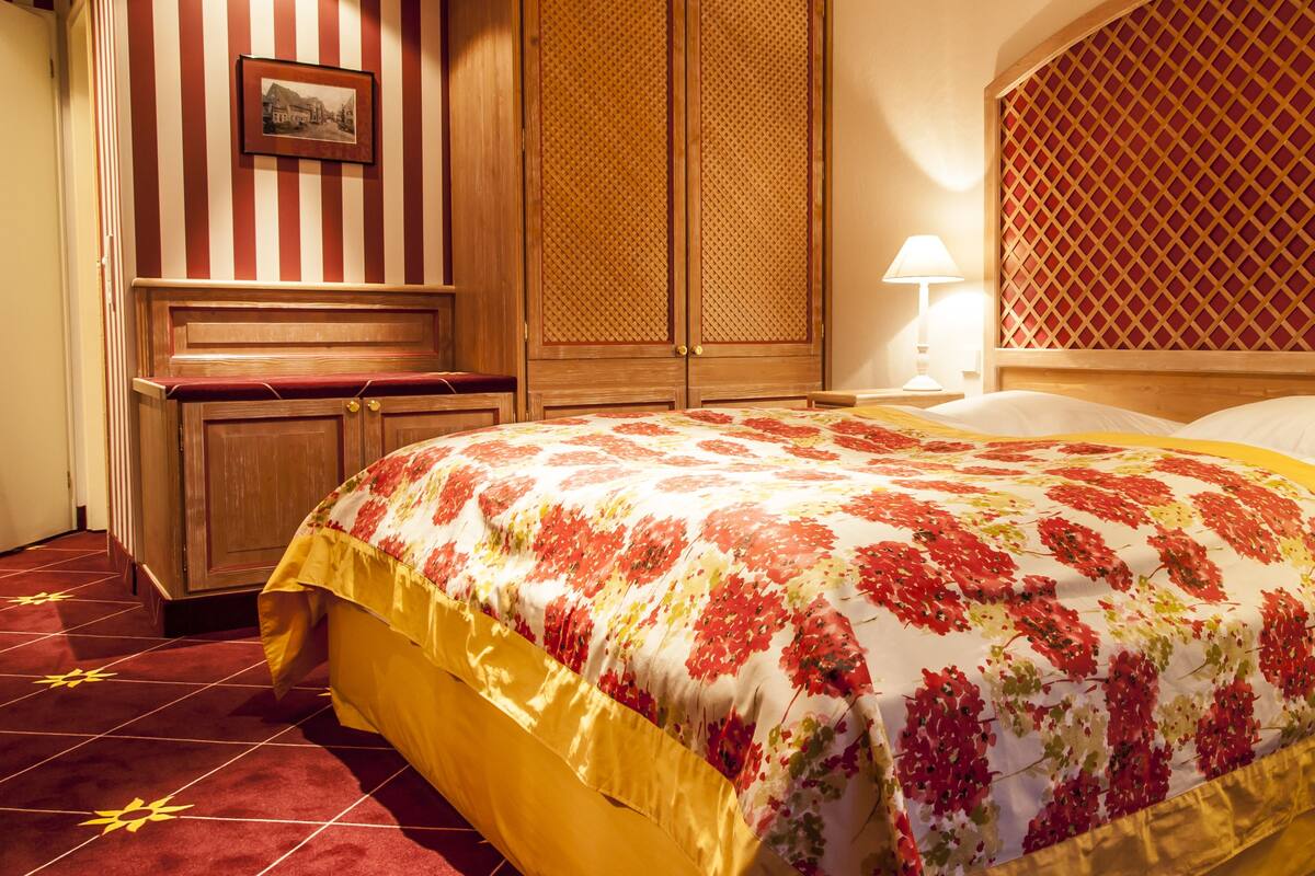 A hotel room with a large bed, wooden wardrobe, and a red and white striped wall.