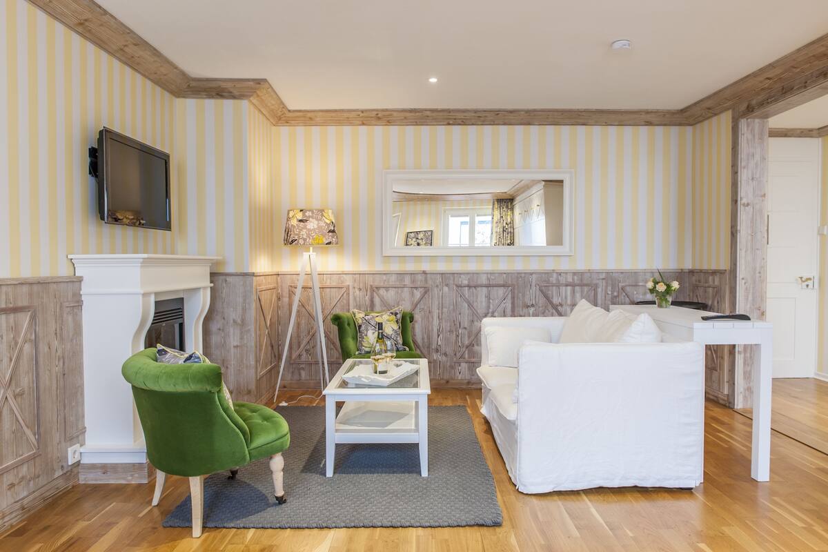 A living room with a green armchair, white sofa, and a fireplace.
