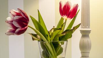 Un florero de vidrio transparente con agua y flores sobre una mesa, junto a una lámpara blanca.
