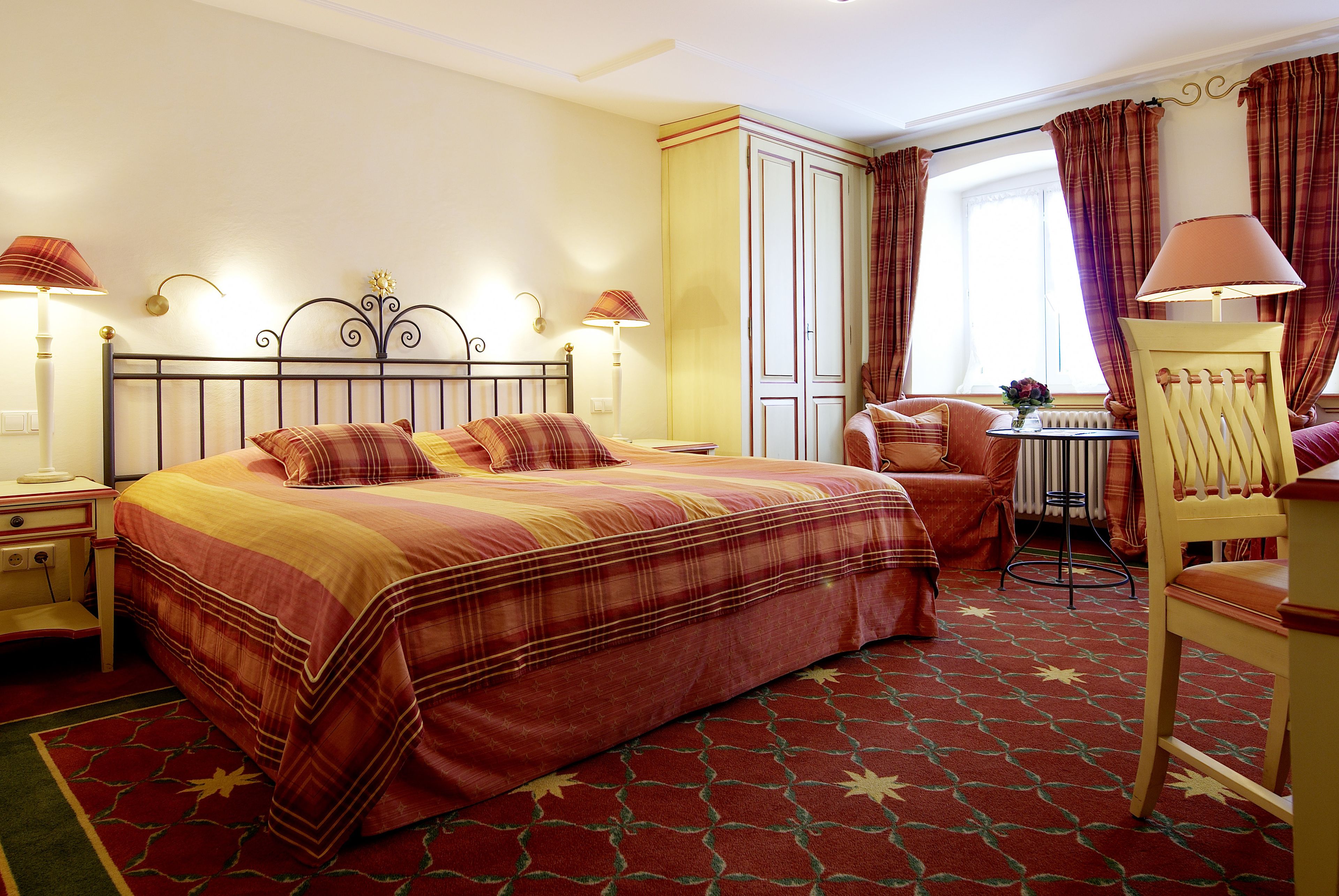 Ein Hotelzimmer mit einem großen Bett, einem Schreibtisch, einem Stuhl und einem Fenster mit Vorhängen.