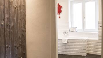 Un baño con puerta de madera, paredes blancas, una bañera blanca y un detalle decorativo rojo.
