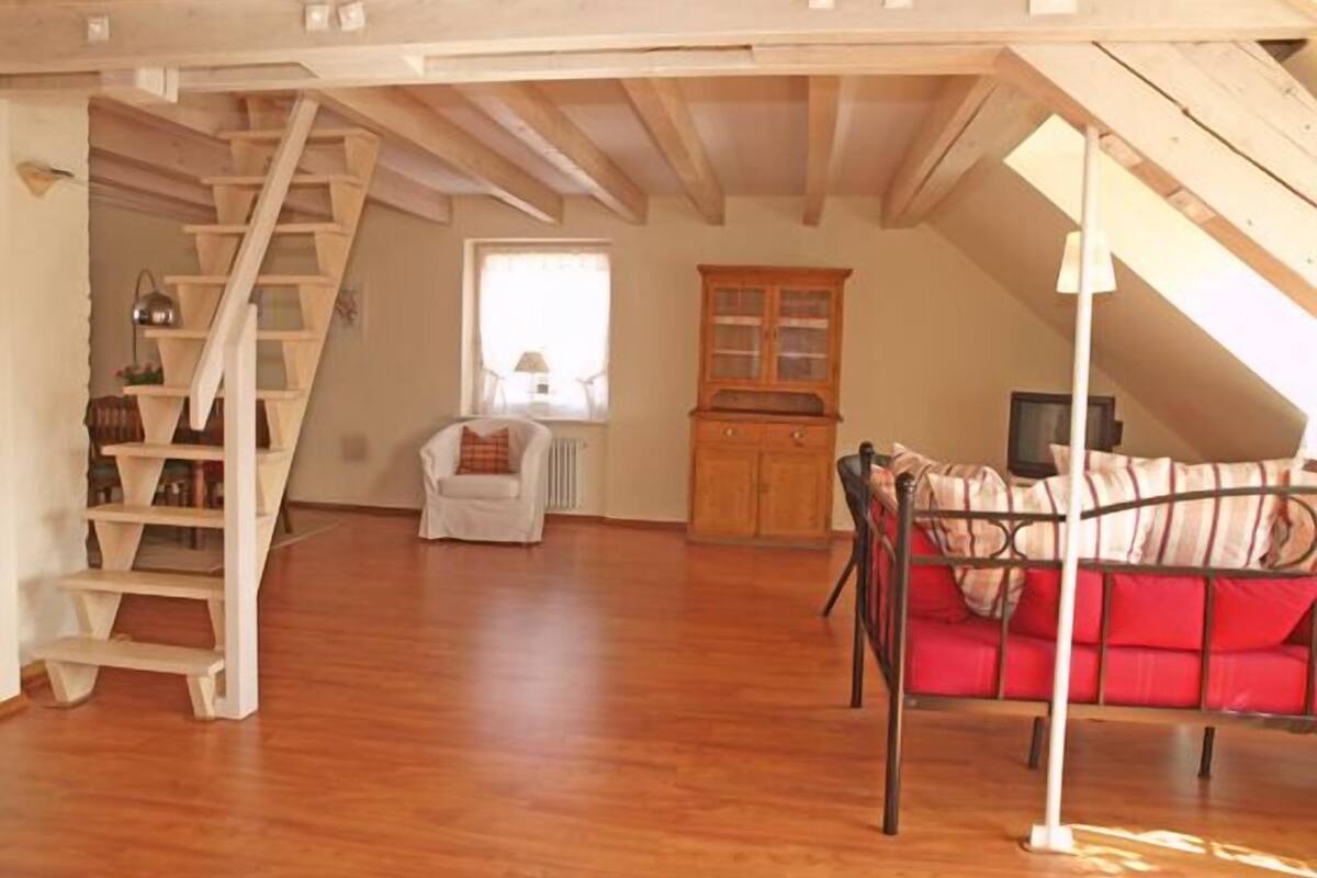 A loft-style room with a wooden staircase, a red sofa, and a wooden cabinet.