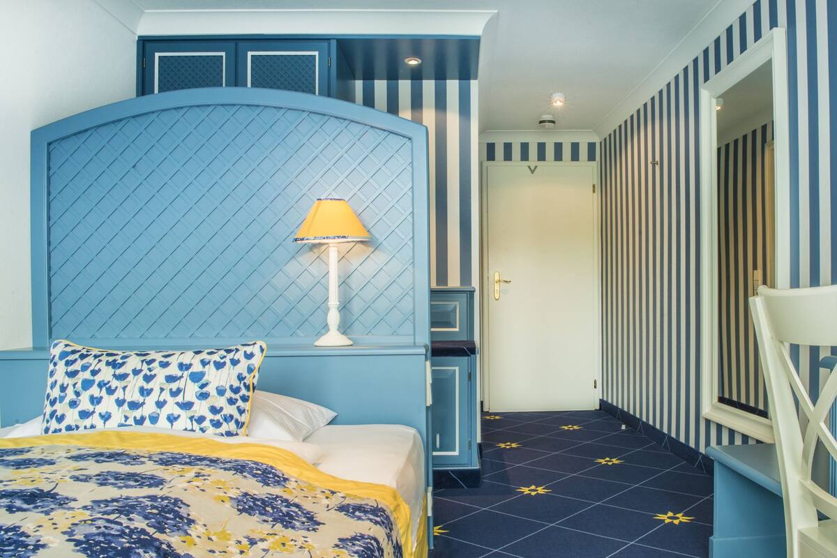 A bedroom with a bed, a nightstand, a lamp, a chair, and a wardrobe.