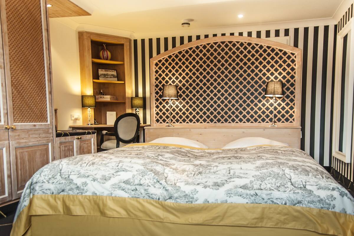 A bedroom with a bed, a desk, and a chair. There is a window with a lattice design and two lamps on either side.