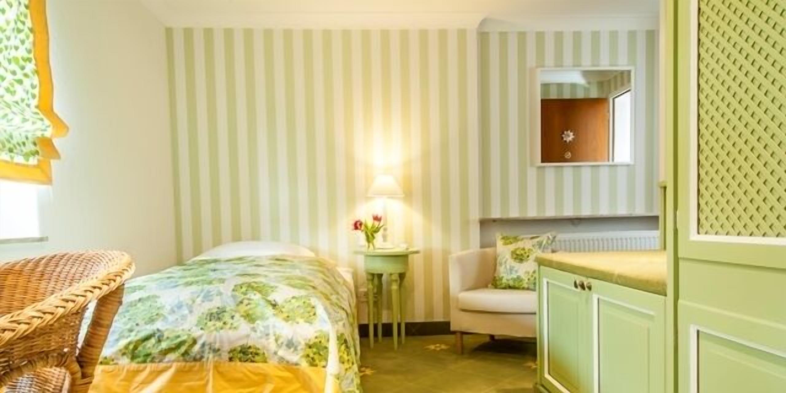 A room with a bed, a chair, a small table with a lamp, and a cabinet.