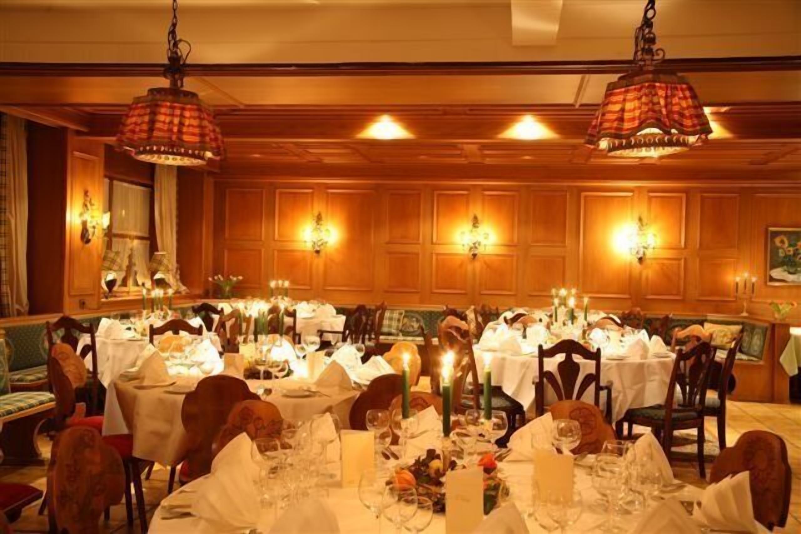 A formal dining room with multiple tables set for a meal, wooden paneling on the walls, and hanging pendant lights.