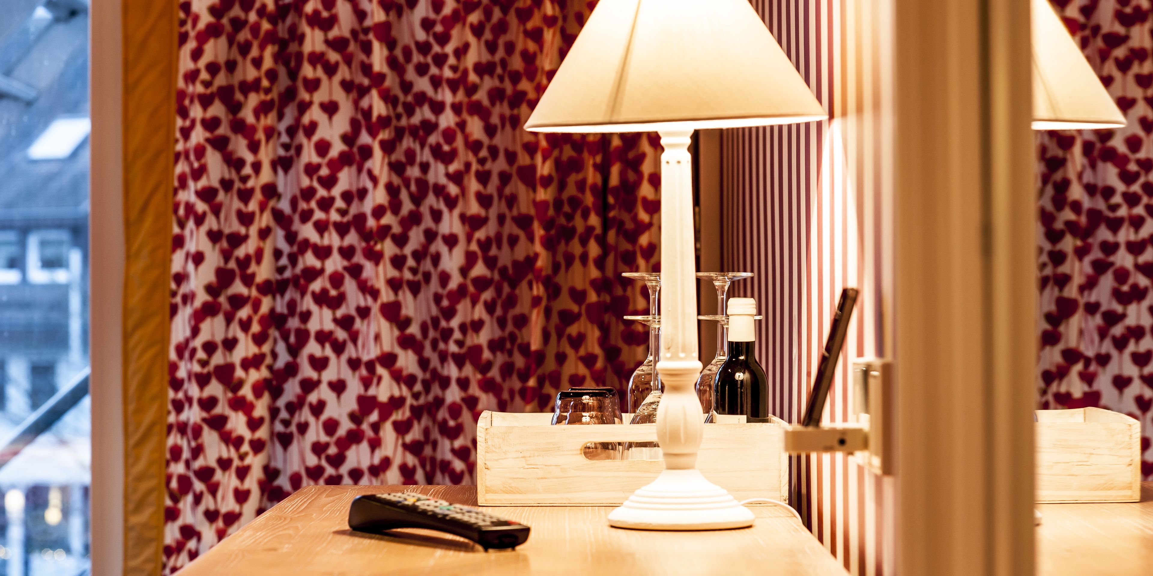A wooden table with a remote control, a lamp, and a bottle of wine.