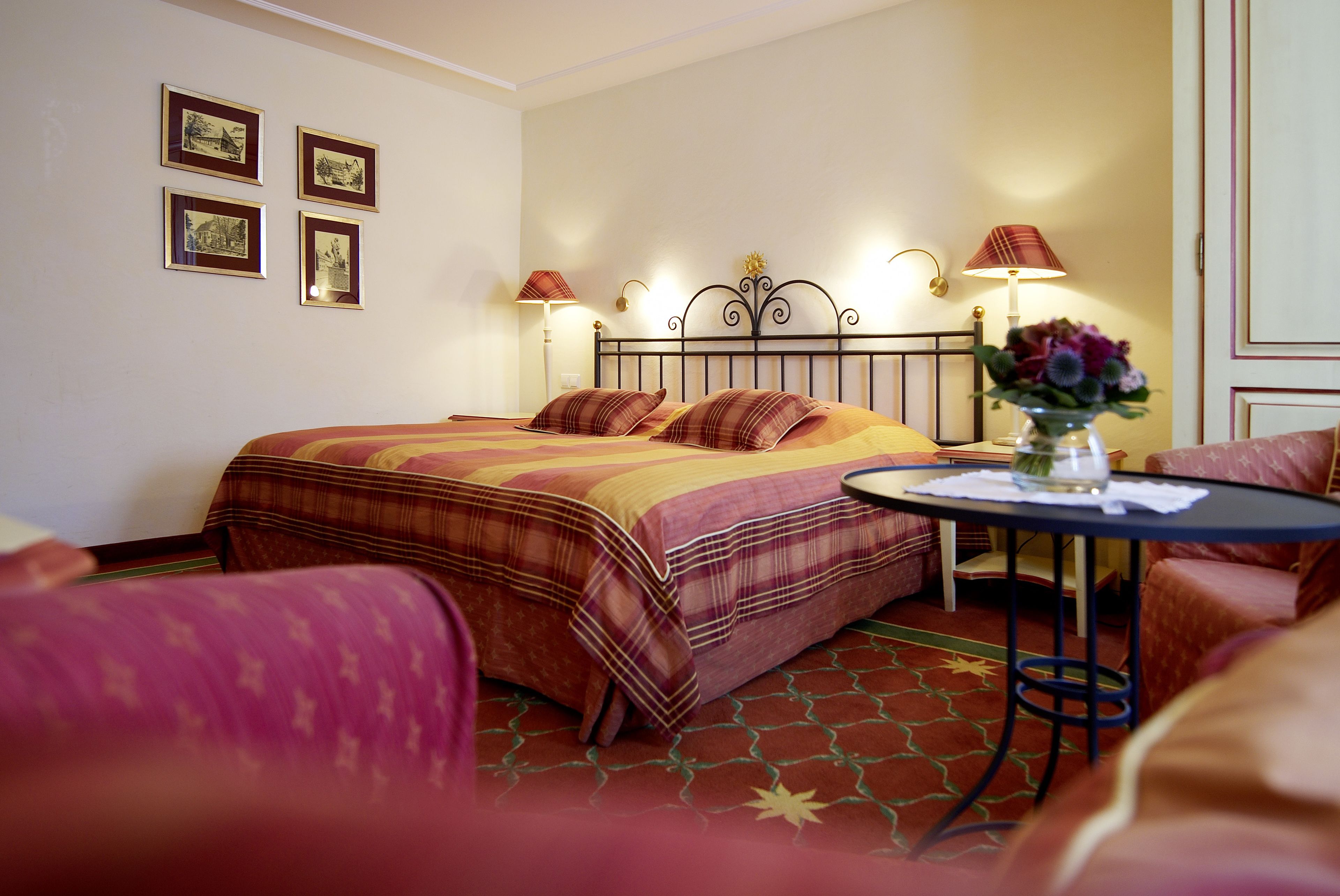 A hotel room with a bed, a small table with a vase of flowers, and a chair.