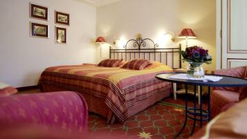 A hotel room with a bed, a small table with a vase of flowers, and a chair.