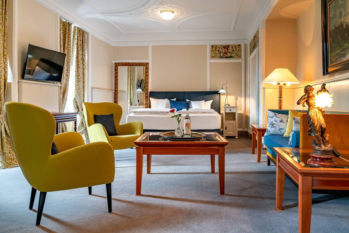 Une chambre d’hôtel avec un lit, une télévision, des chaises jaunes, une table basse et une statue.