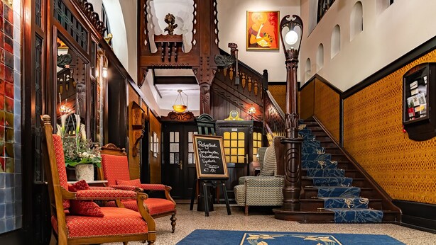 Un hall d’entrée avec un escalier, des fauteuils à revêtement rouge, un tableau noir affichant le menu et une moquette à motifs.