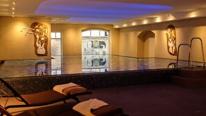 Un espace spa doté d’un jacuzzi à ciel ouvert, de chaises longues et d’un mur décoré de mosaïques.