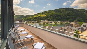 Un balcon avec des fauteuils et des tables, donnant sur une rivière et une ville.