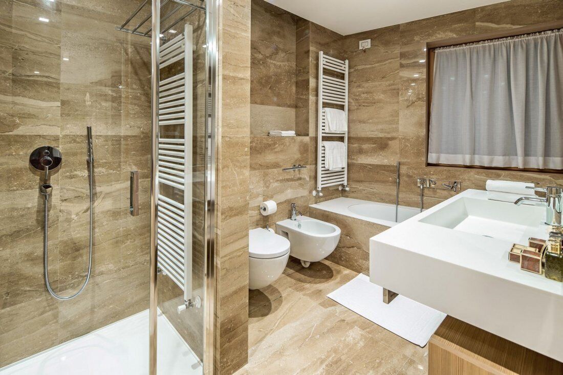 A modern bathroom with a glass-enclosed shower, a bidet, a bathtub, and a large vanity with a mirror.