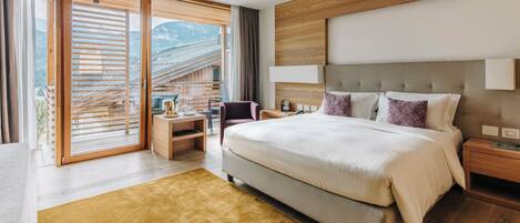 A modern bedroom with a large bed, wooden headboard, and a view of mountains through the sliding glass door.