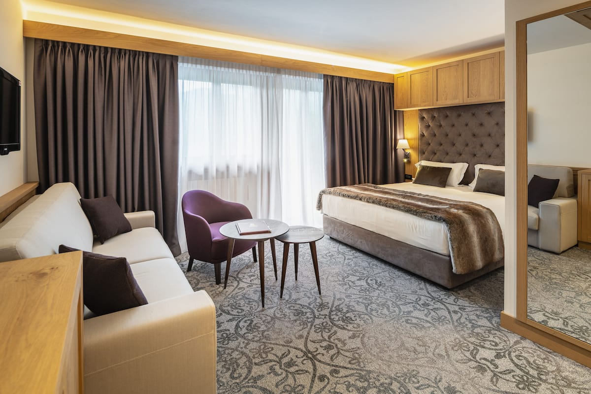 A hotel room with a bed, a sofa, a chair, a small table, and a mirror.